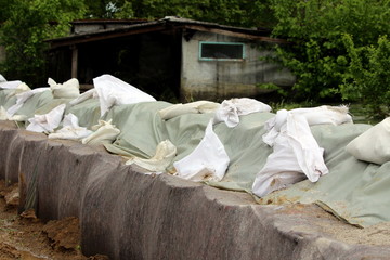 Line of temporary flood protection wall made of box barriers and sandbags covered with thick geotextile fabric and nylon used to protect family houses from massive floods on heavy rain days with small