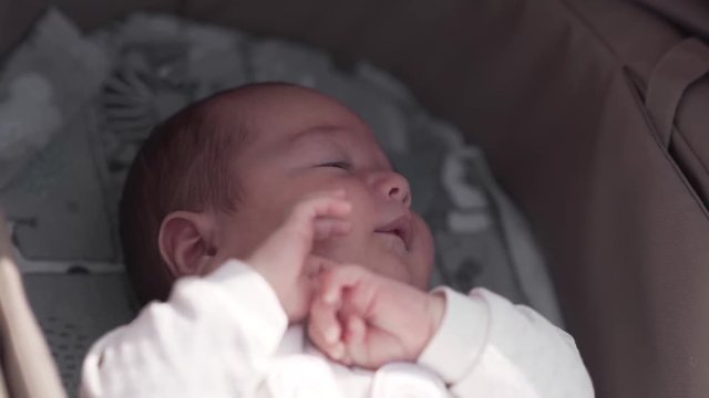 Cute little three months baby is laying in a carriage and trying to sleep.