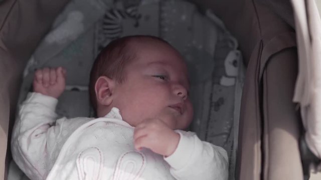 Cute little three months baby is laying in a carriage and trying to sleep.