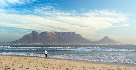 Man is running at sand beach on background of Table Mountain, Cape Town