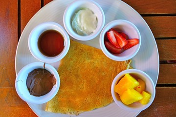 A crepe with assorted fruit and chocolate toppings on a breakfast plate