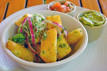 Bowl of yucca fries with parsley and garlic sauce and side dishes of guacamole and salsa