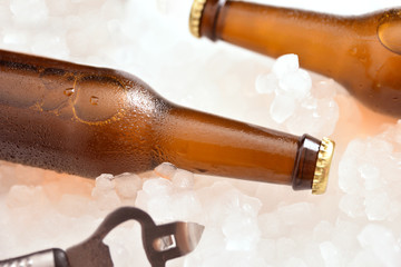 Two beer bottles lying on crushed ice with bottle opener