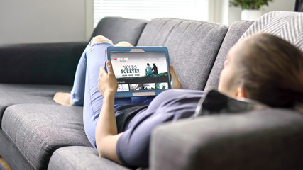 Woman choosing movie from online stream service with tablet. Watching series with on demand video...