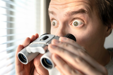 Surprised man with binoculars. Curious guy with big eyes. Nosy neighbour stalking or snooping secrets, gossip and rumour. Silly funny face. Shocked about unbelievable news. Stalker peeping people. - obrazy, fototapety, plakaty