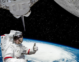 Astronaut gives thumbs-up, earth and planet with craters like moon. The elements of this image...