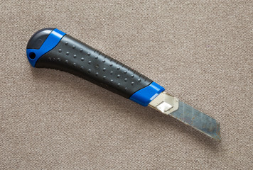 Close-up of isolated stationery retractable metallic knife with sharp blade on light cloth copy...