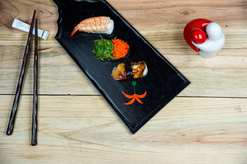 Lovely beautiful delicious tradional Japanese sushi food sets served on black wood tray with chopsticks on bright wooden table background.