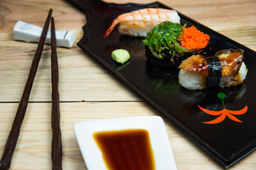 Obraz na płótnie Canvas Traditional Japanese sushi sets served on black wood tray,with chopsticks on bright wooden table background.