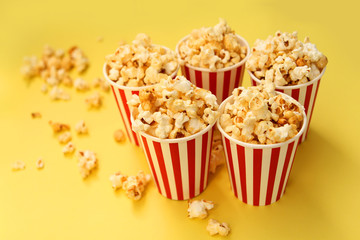 five red-and-white paper cups with popcorn on a yellow background, several pieces are scattered nearby
