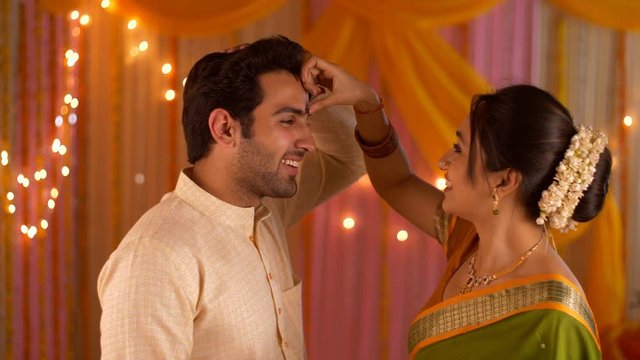 Beautiful wife putting tilak of husband's forehead - Hindu Customs. Happy Indian couple celebrating festival. Indian stock footage of young woman putting tilak on husband's forehead during festivities