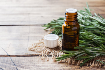 Rosemary essential oil in a glass bottle with fresh branch rosemary herb on wooden table for spa,aromatherapy and bodycare.Copy space.