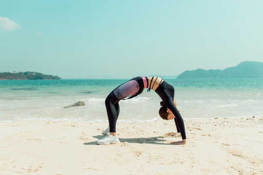 Fit woman making stretching gymnastic at the beach. Beautiful woman doing yoga in the hot summer day. Phuket. Thailand
