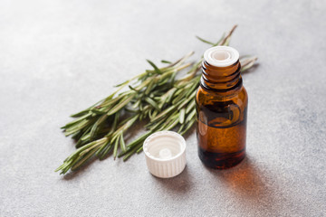 Rosemary essential oil in a glass bottle with fresh branch rosemary herb on grey table for spa,aromatherapy and bodycare.Copy space.