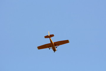 Small dark yellow plane used for panoramic flights flying high in air above local urban area on clear blue sky background