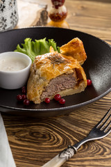 Beef wellington with cranberry and white sauce on wooden table