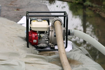 Small industrial petrol water pump with strong black metal frame left on top of improvised sandbags...