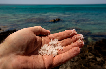 naturbelassenes grobes Meersalz am Strand von der Sonne  getrocknet, in der Hand gehalten vor blaugrünem Meer