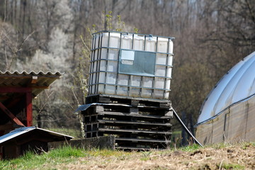 Tilted white intermediate bulk container or IBC plastic tank with metal cage put on top of wooden...