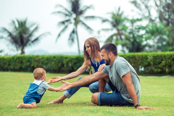 Group Portrait of cute young family. Baby crawling on green grass lawn during walk with her parents. Happy childhood and baby healthcare. baby crawls to parents