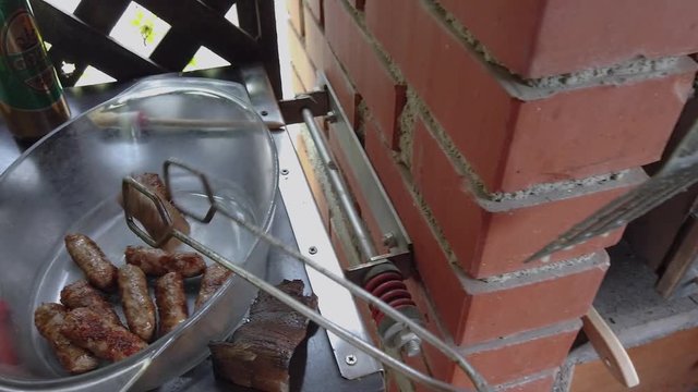 Male hand taking off grill finished minced meat rolls cevapcici in glass bowl. Filmed while grilling mixed meat with vegetables on charcoal grill.