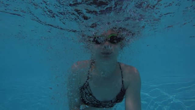 A European woman in a swimsuit and swimming glasses jumps into the pool shooting herself on the action camera, shooting while jumping and under water