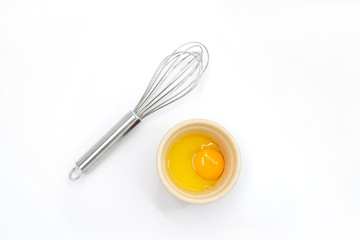 Top view of an egg yolk and whisk on a white background