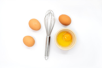 Eggs, a whisk and one egg yolk on a white background