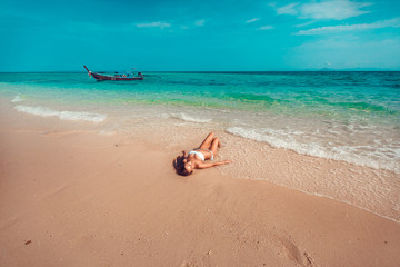 Fototapeta na wymiar Young and pretty girl model in a bikini sunbathing on the beach resort of the Andaman sea. Boat and blue sea background.