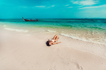 Fototapeta na wymiar Young and pretty girl model in a bikini sunbathing on the beach resort of the Andaman sea. Boat and blue sea background
