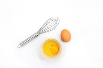 Top view of an egg, egg yolk and whisk on a white background