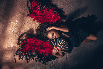 Fashion portrait of a passion woman wearing black dress with red angel wings and with black fan in...