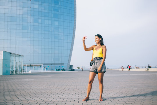 Positive hipster girl posing and clicking selfie photo on smartphone front camera enjoying summer trip for discover world, happy millennial female tourist taking pictures via mobile phone