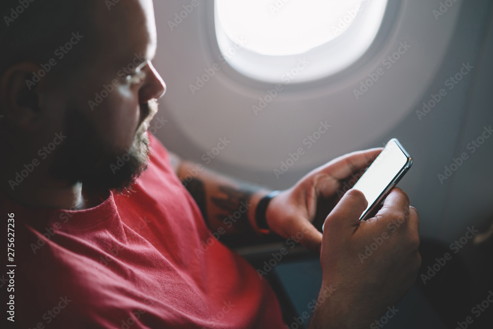 Poster back view of young man flight passenger connecting to wireless internet on board while sitting next 
