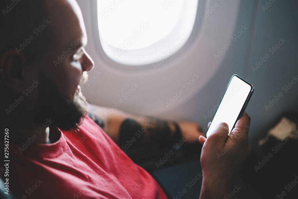 Poster back view of young man flight passenger connecting to wireless internet on board while sitting next 