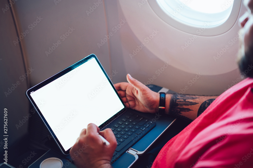 Poster young man flight passenger connecting to wireless internet on board with touch pad while sitting nex