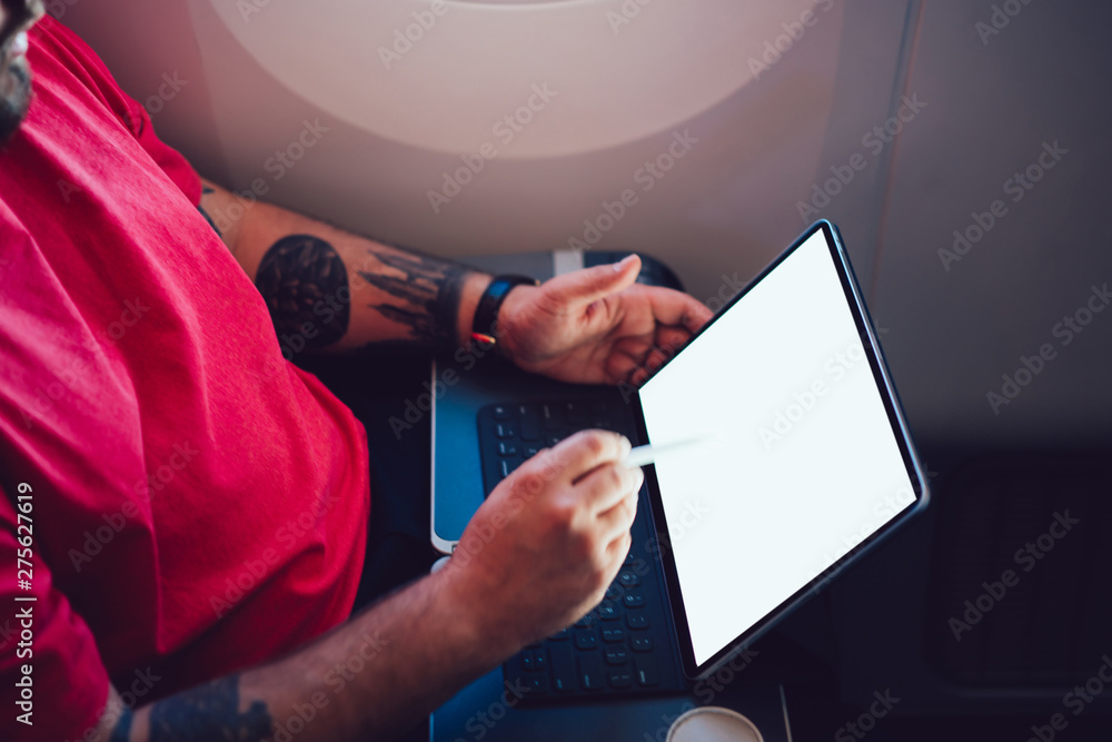 Poster young man flight passenger connecting to wireless internet on board with touch pad while sitting nex