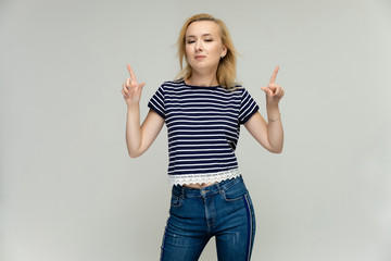 Portrait of a pretty interesting blonde girl on a white background in jeans and a striped blue t-shirt. Standing in front of the camera, smiling, showing hands. Shows a lot of emotions.