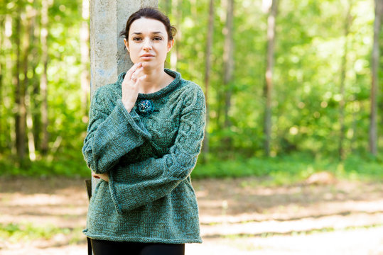The beautiful brunette poses in the park in a green knitted pullover