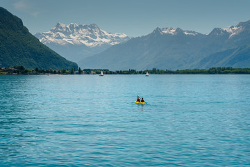 Swiss Alps mountain and Lake Geneva landscape with tourist paddling on the lake in a yellow kayak