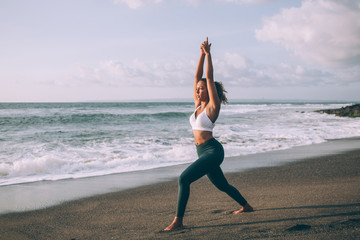 Young attractive woman practicing yoga standing in Warrior one exercise enjoying time for calmness, female fit girl in casual tracksuit practising Virabhadrasana I pose during working out