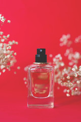 A jar of perfume on a red background with gypsophila.