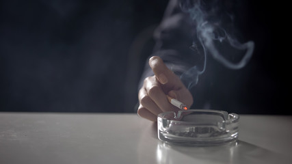 Female hand holding burning cigarette under ashtray, nicotine addiction concept
