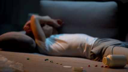 Depressed teenager lying on sofa, medication overdose, painkillers pile on table