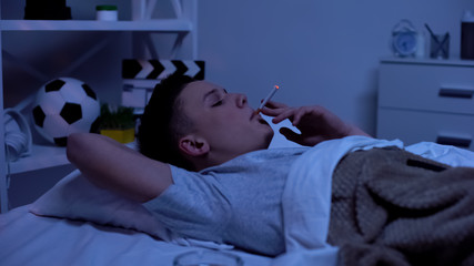 Nicotine addicted teenager smoking in bed, harmful habit, risk of accident