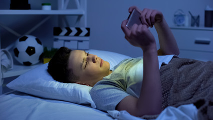 Teenager watching video on smartphone, evening relaxation, gadget addiction