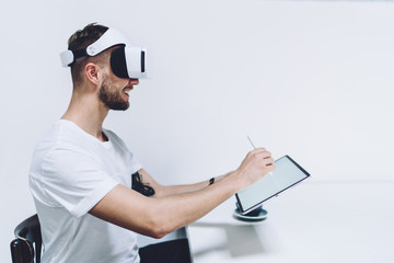 Side view of cheerful male trying virtual reality headset glasses for testing VR environment,...