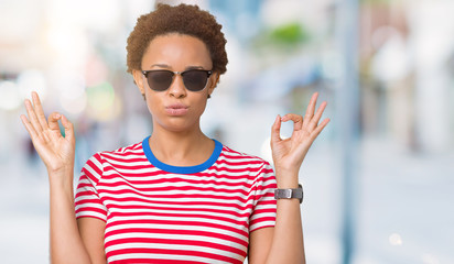 Beautiful young african american woman wearing sunglasses over isolated background relax and smiling with eyes closed doing meditation gesture with fingers. Yoga concept.