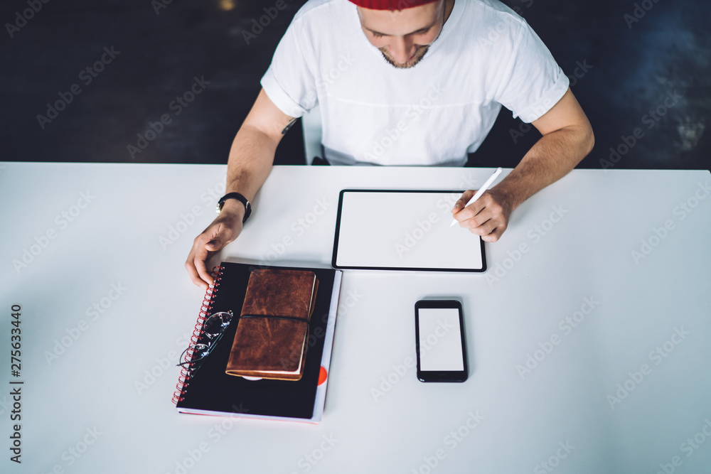 Poster top view of millennial hipster guy sitting at desktop with blank tablet with copy space area for art