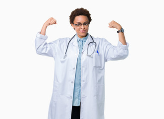 Young african american doctor woman wearing medical coat over isolated background showing arms muscles smiling proud. Fitness concept.